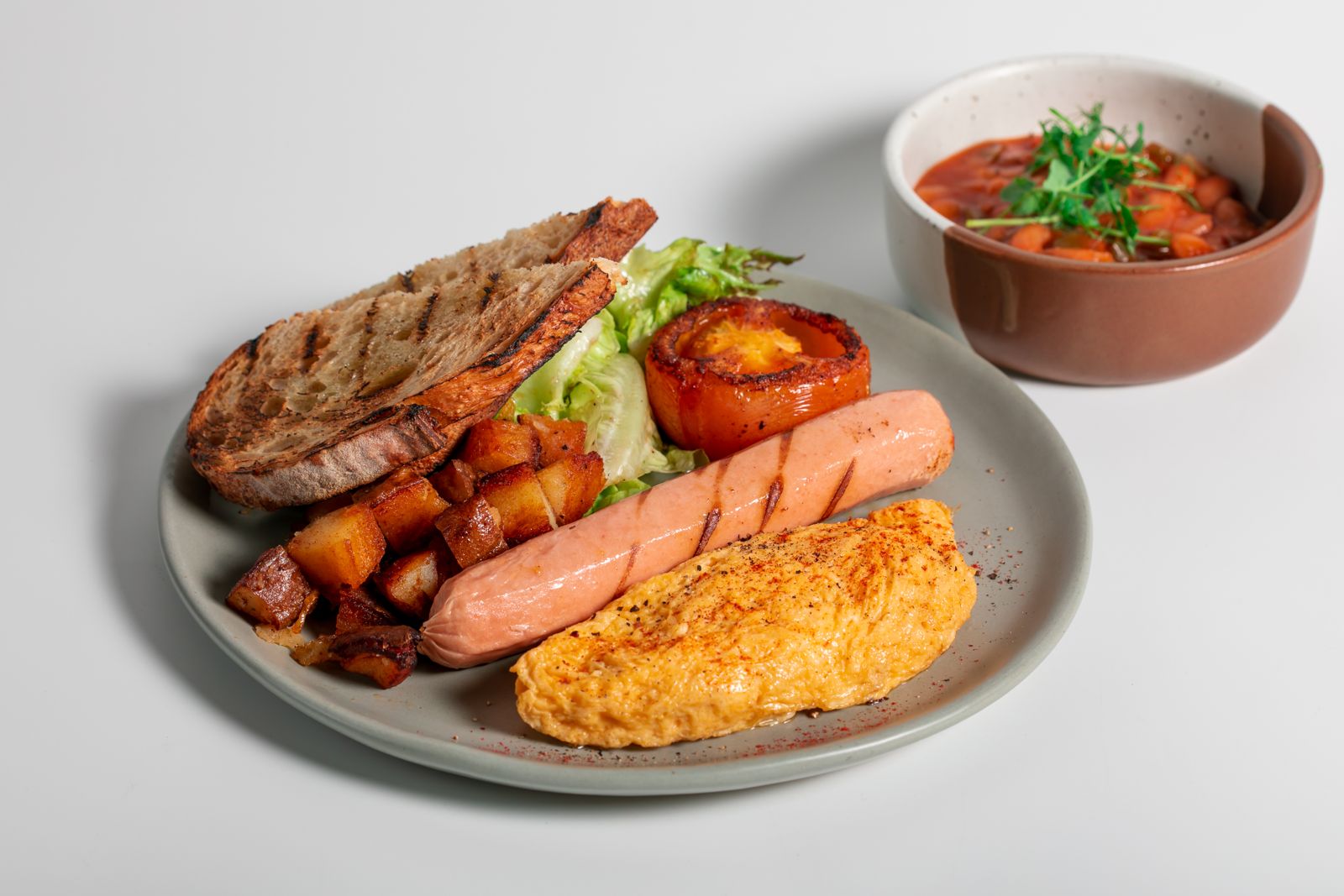 Cliche Eggs with butter & mozza omelette, sausages, hash and charred tomato